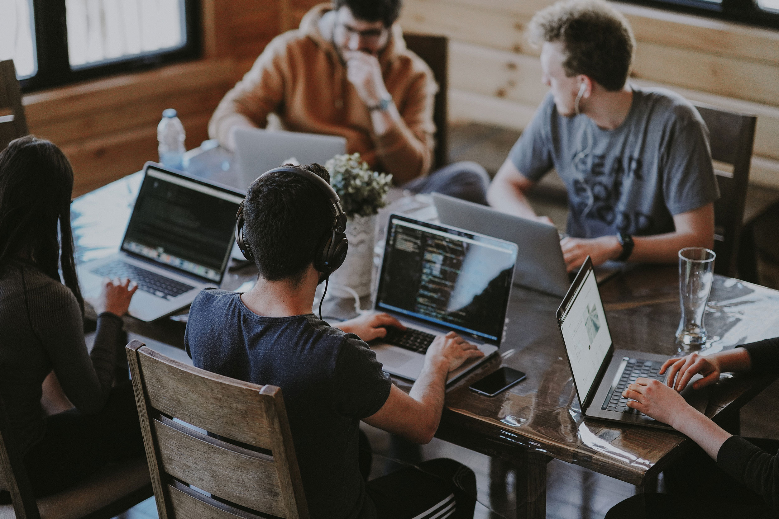 photo of a group of young adults sitting at table working on laptops